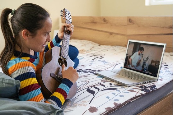 Women playing guitar with man online.