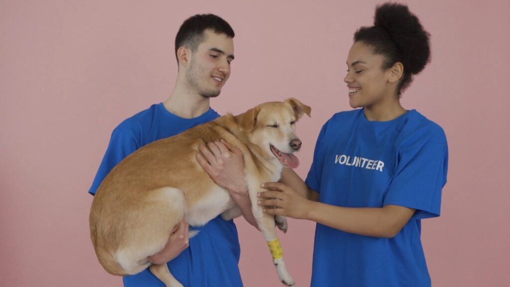 two smiling animal shelter volunteers holding a dog